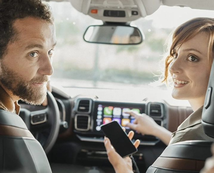 Pareja en el interior de un coche utilizando el móvil y la pantalla multimedia